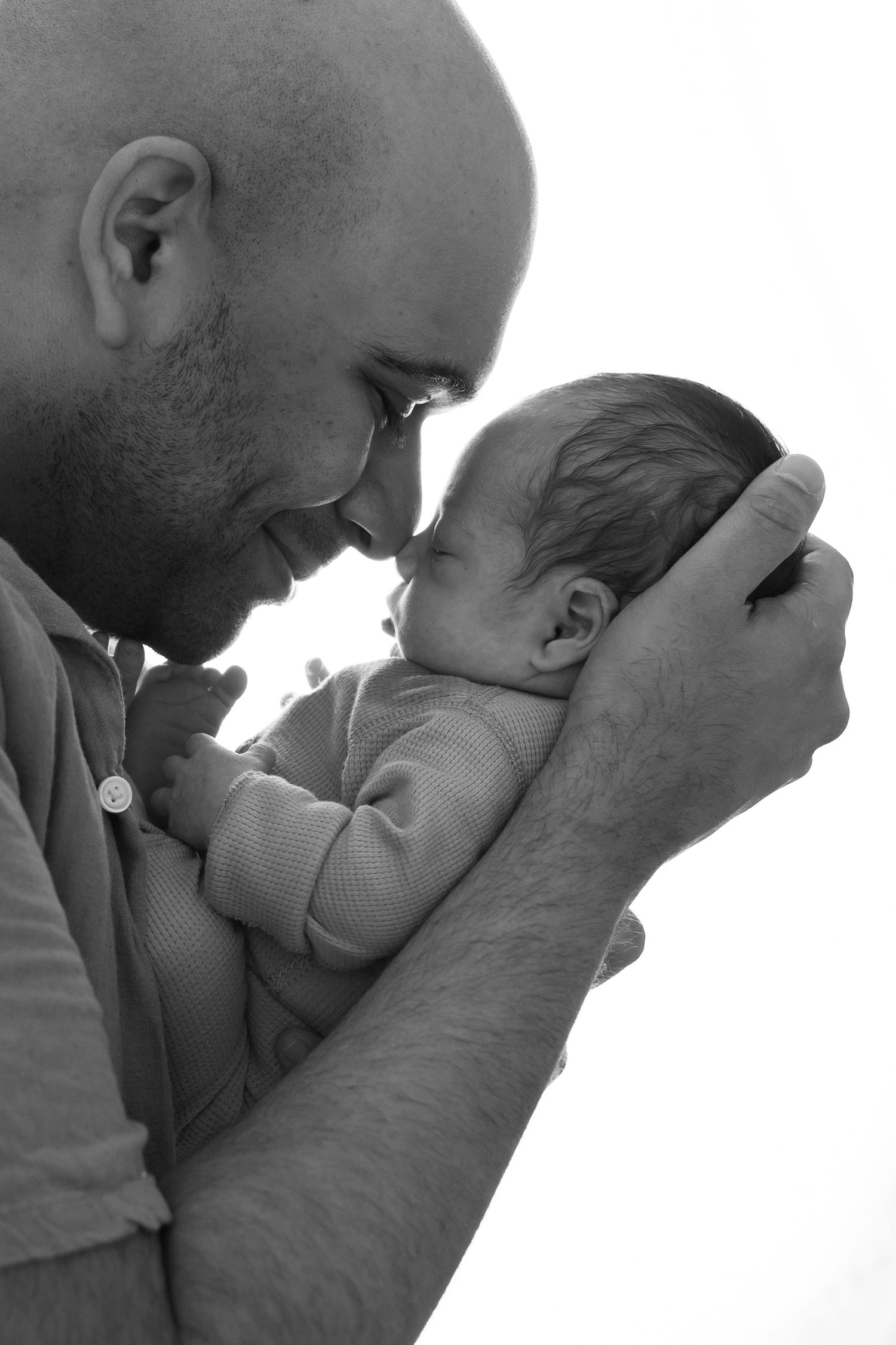 A tender black and white portrait of an adult and newborn sharing an intimate moment together.