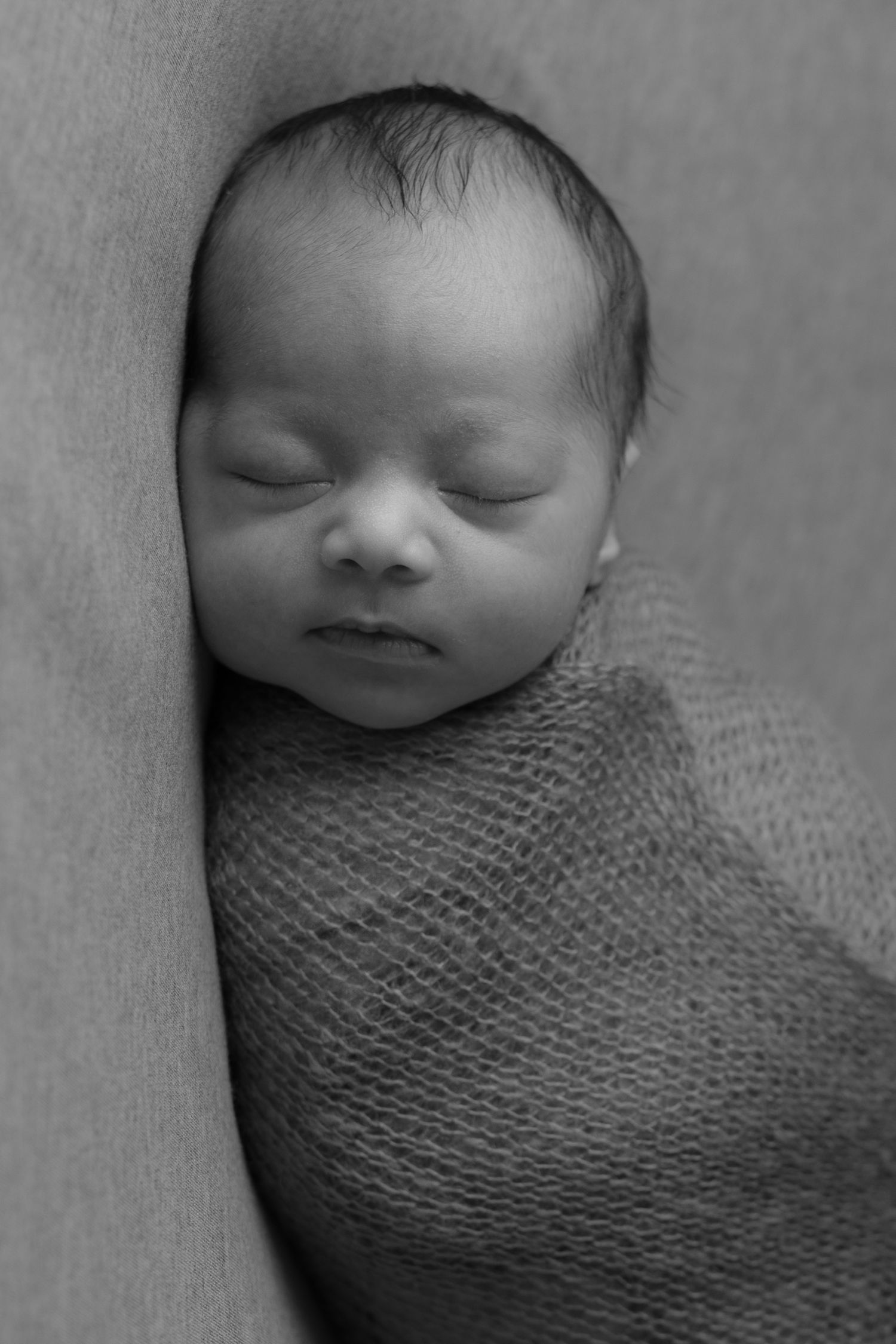 Black and white portrait of a peaceful sleeping newborn baby swaddled in a knit blanket.