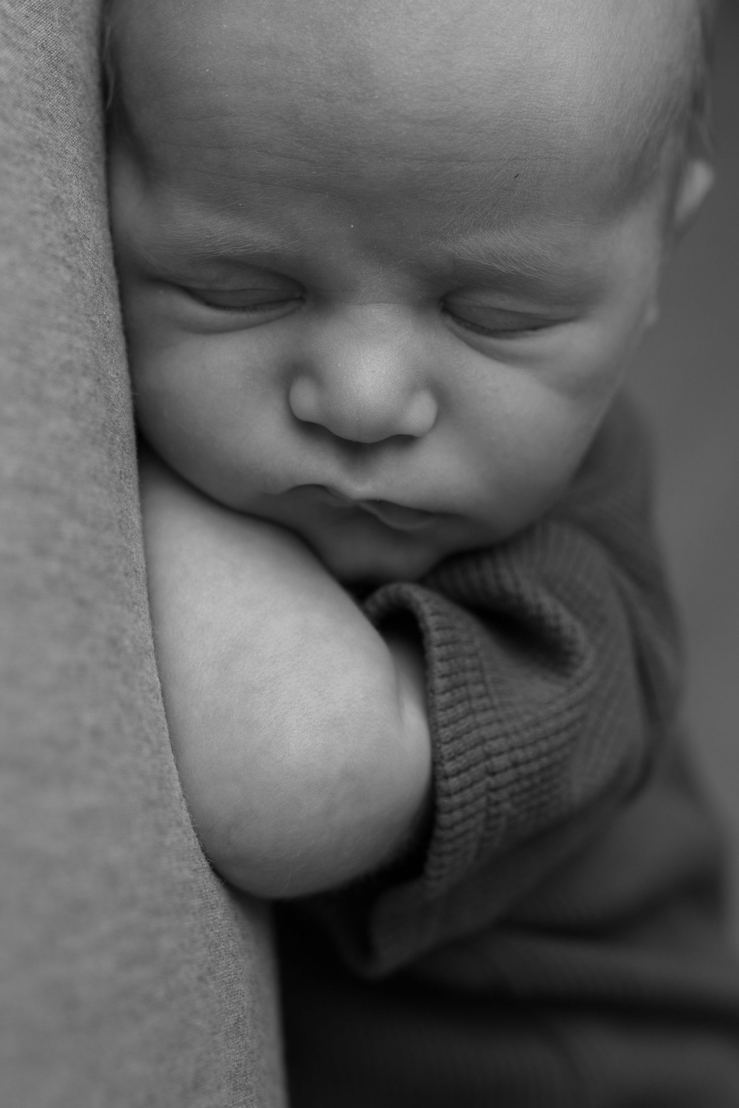 Black and white close-up series showing a sleeping baby's peaceful expression and tiny fingers against a soft blanket.