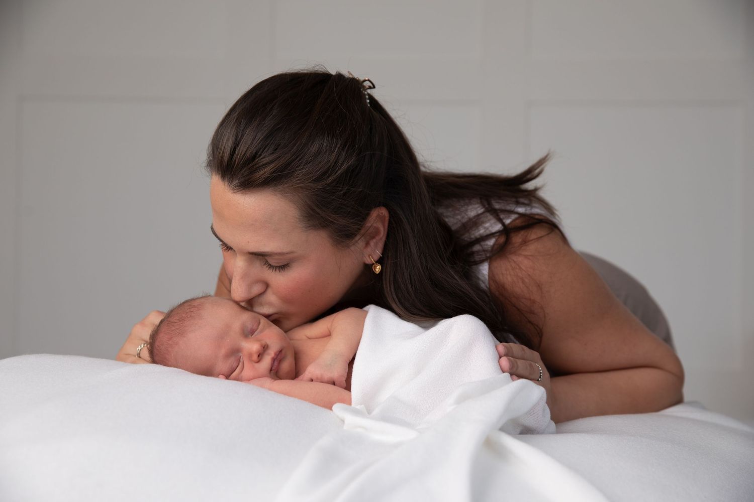 A tender moment between parent and newborn baby lying on white bedding.