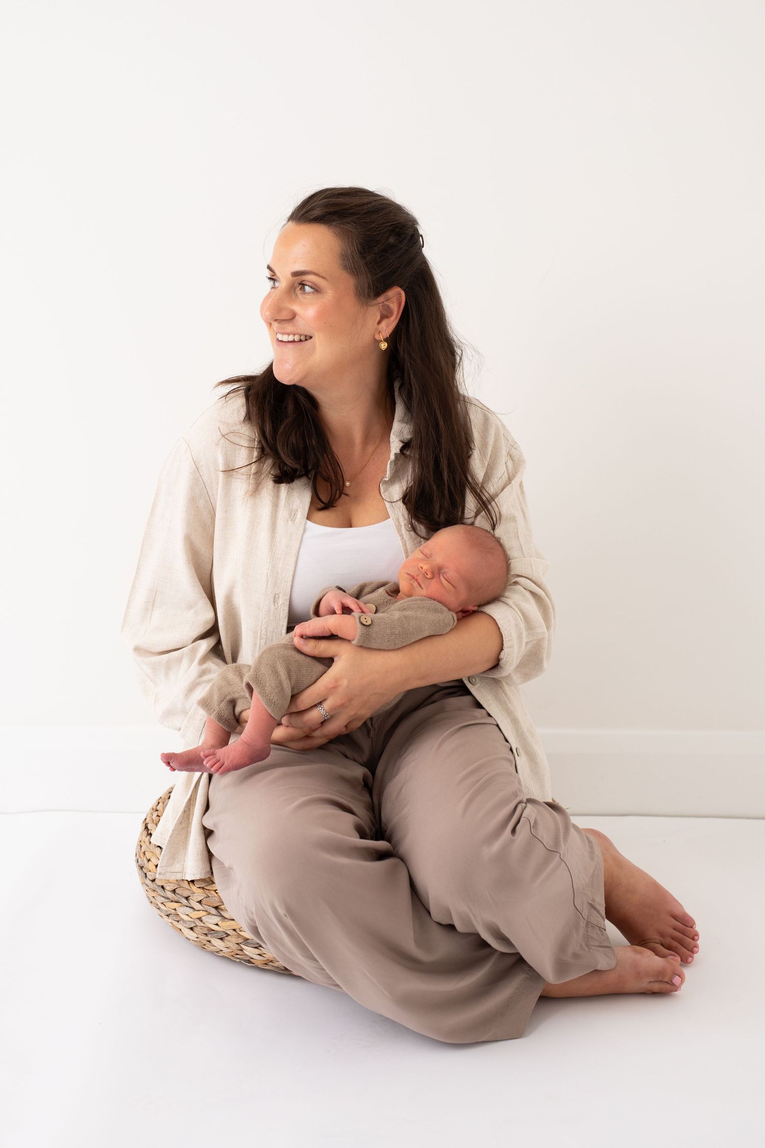 A tender moment captured of a parent holding a newborn baby while sitting on a woven basket against a white backdrop.