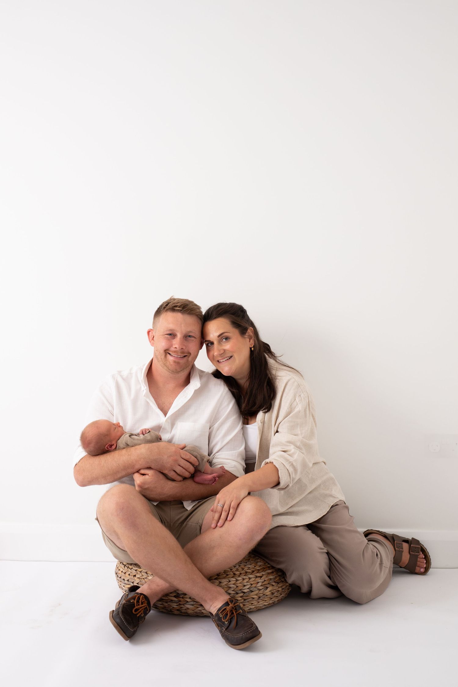 A family portrait with parents sitting together on a woven basket seat, cradling their newborn baby.