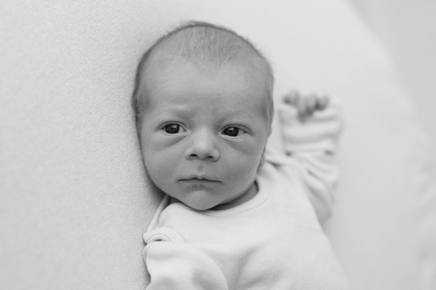 Black and white portrait of a newborn baby in white clothing against light background.