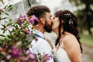 A romantic golden hour kiss between couple framed by purple blooming flowers during an outdoor photo session.