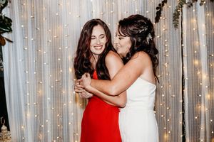 Two people embrace and smile while standing in front of a white curtain with glowing string lights.