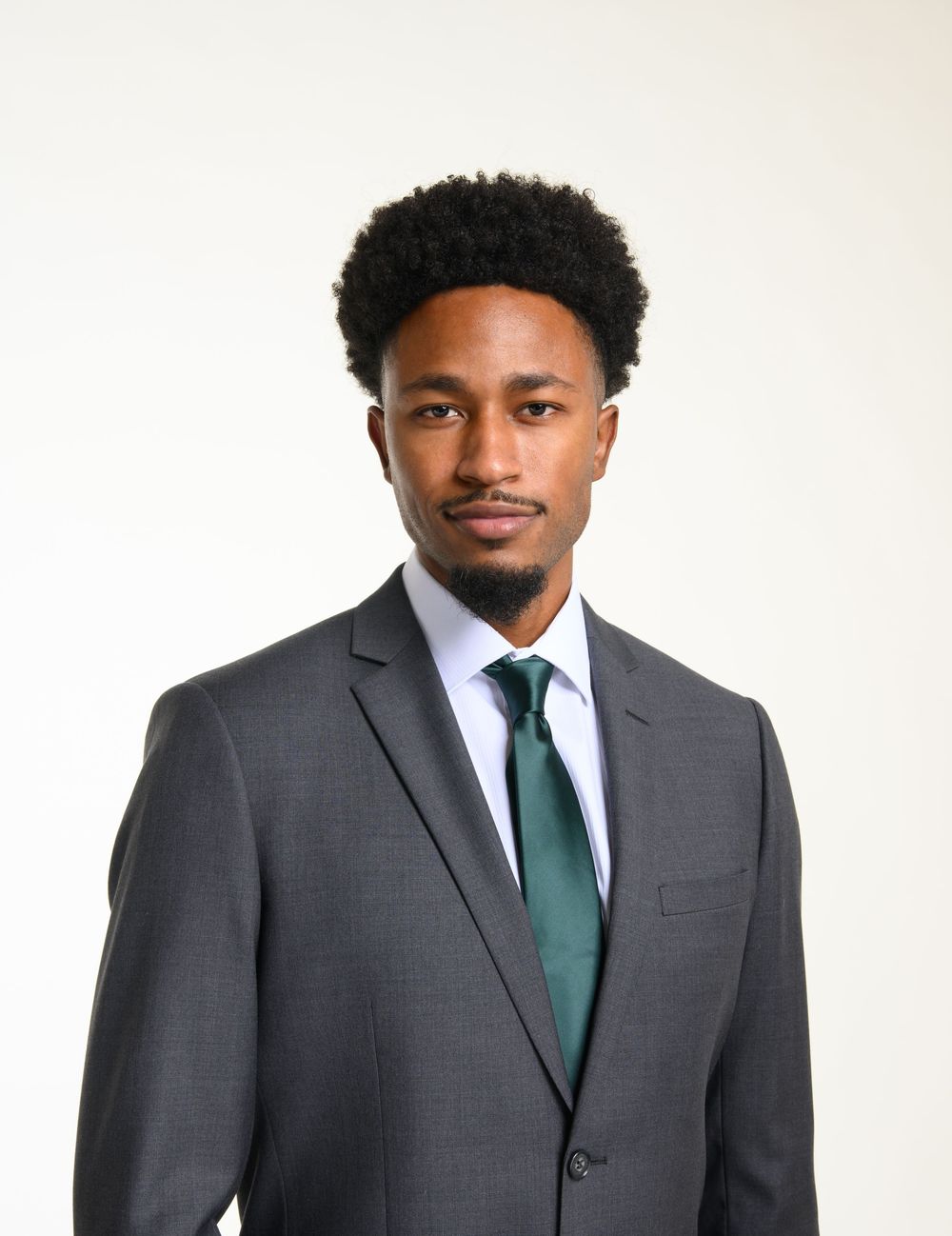 Professional young man in gray suit and green tie poses for formal headshot portrait.
