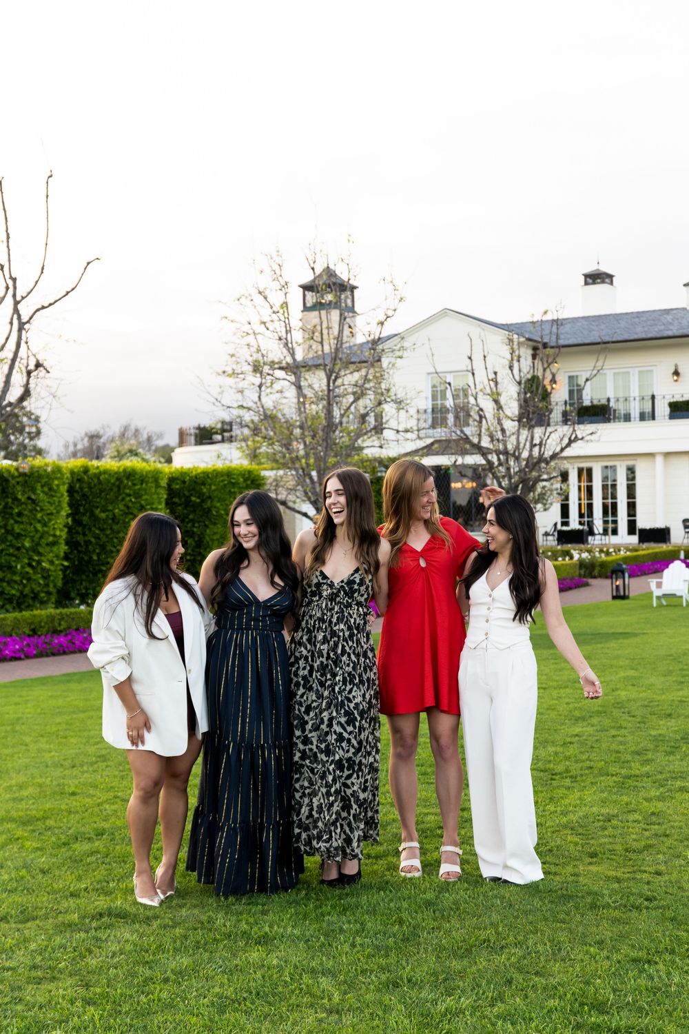 A group of friends in formal attire stand together on a green lawn during a special occasion.