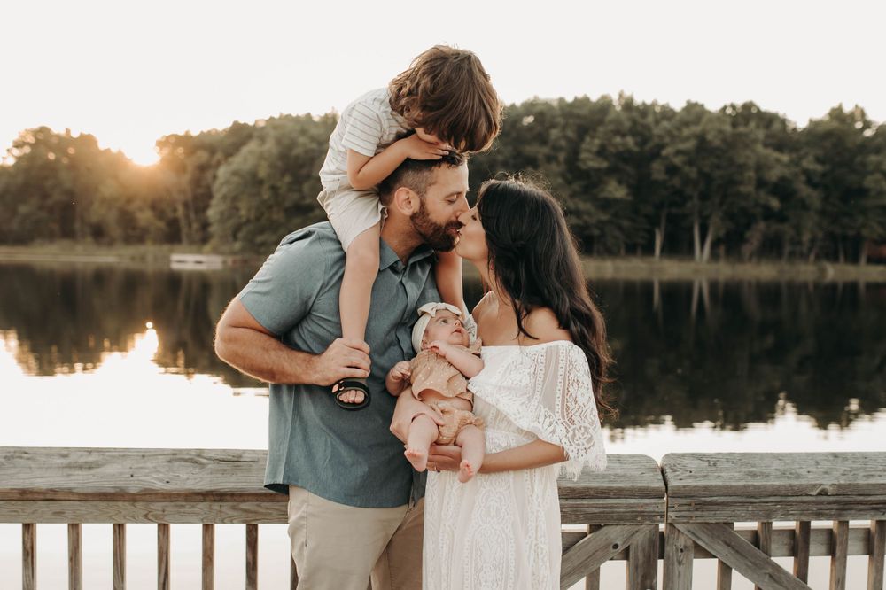 Family of four shares a sweet kiss at golden hour on a lakeside dock.