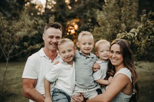 Smiling family of five outdoors, father and mother holding three young boys in casual summer clothing.