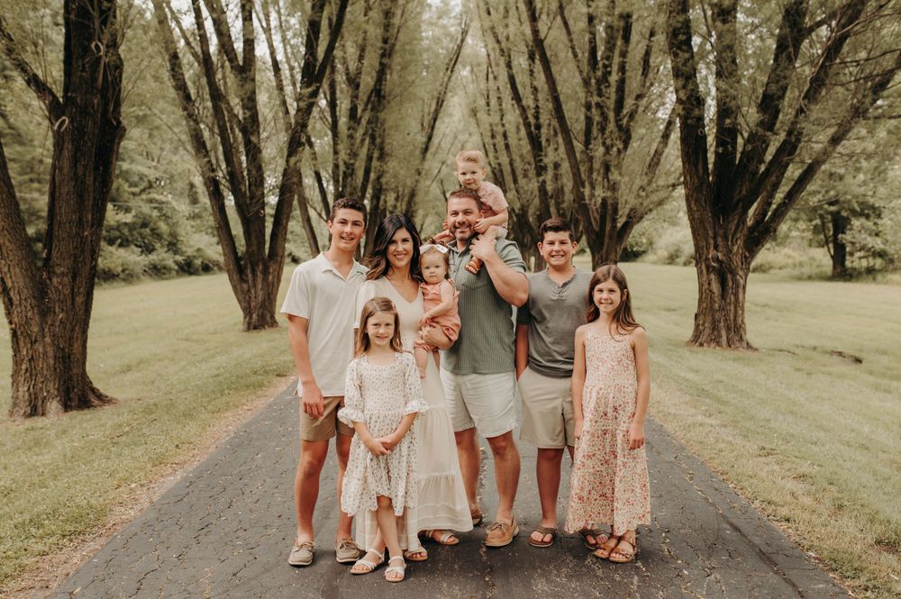 Large family of eight posing together on a tree-lined path in summer.
