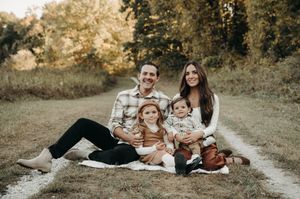 Smiling family of four sitting together on a blanket in a golden autumn meadow for portraits.