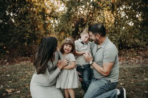 Happy family of four laughing together during an outdoor fall family portrait session in the park.