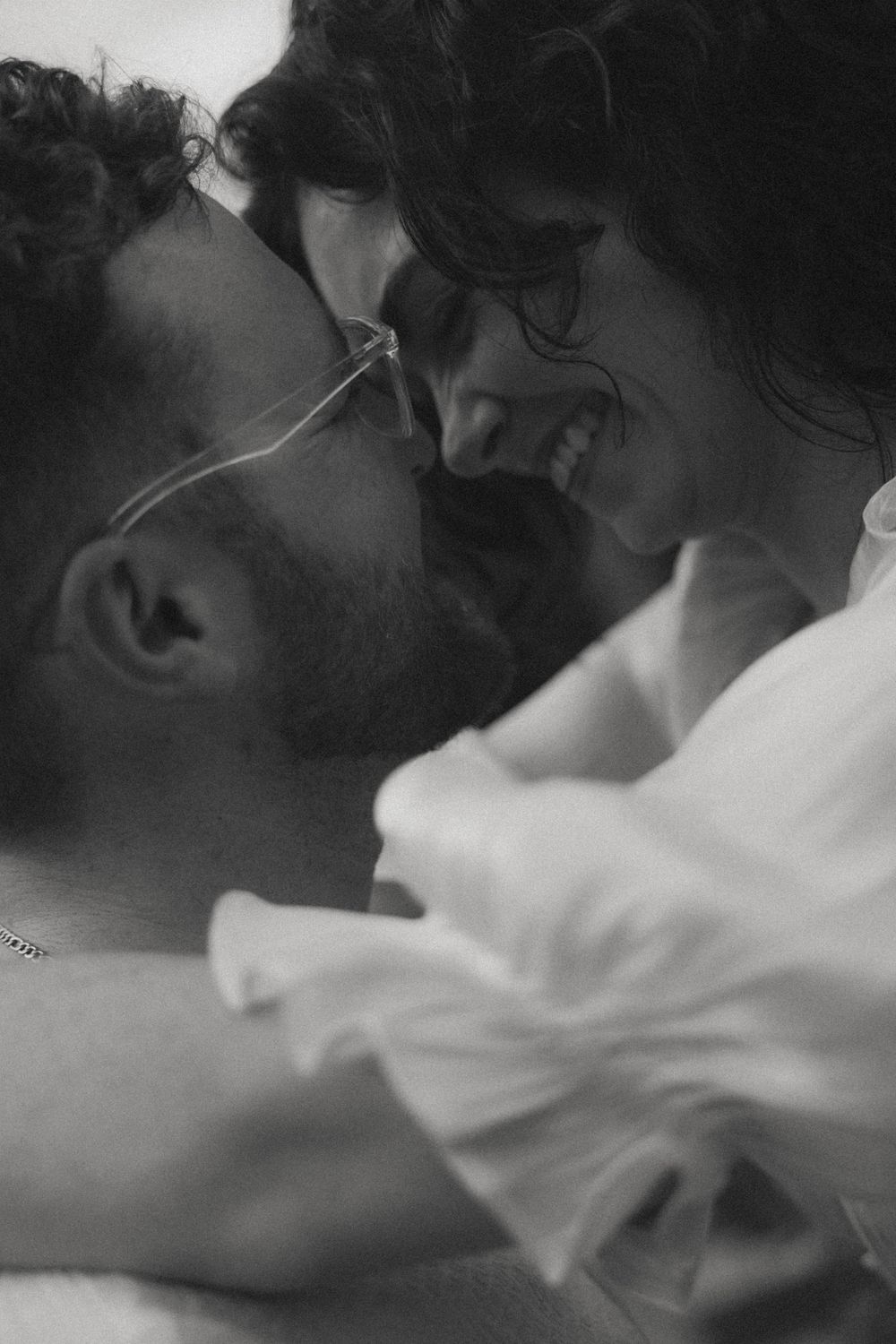 Black and white photo of a couple sharing an intimate moment, smiling and leaning close together.