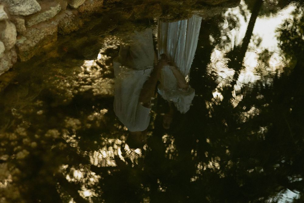 A person in a white dress stands near a stone wall surrounded by lush green trees in a dreamy, inverted composition.
