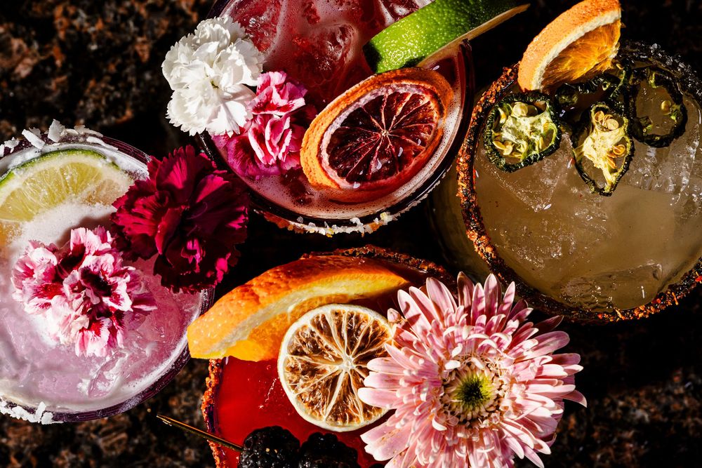 Overhead view of artisanal cocktails decorated with fresh flowers and citrus garnishes.
