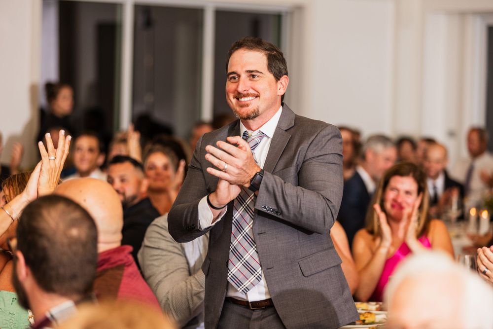 A joyful participant claps enthusiastically during an indoor event with a crowd in the background.