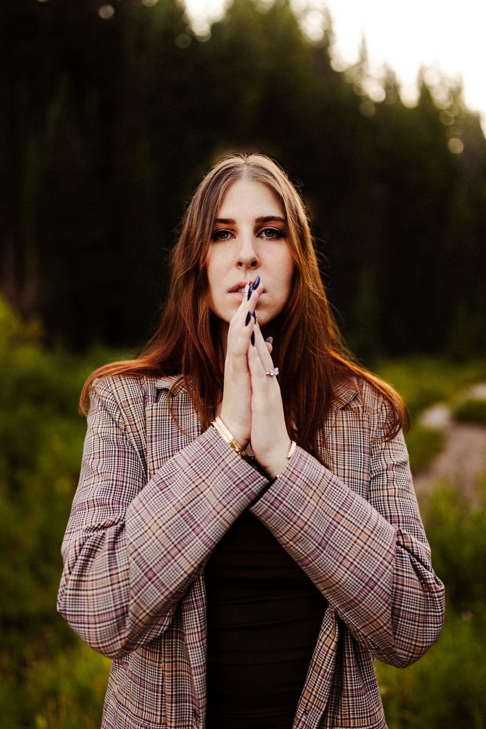 Contemplative pose in plaid blazer against forest backdrop at dusk.