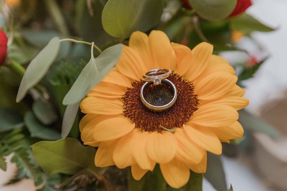 Wedding rings displayed on top of a bright orange sunflower in a floral arrangement.