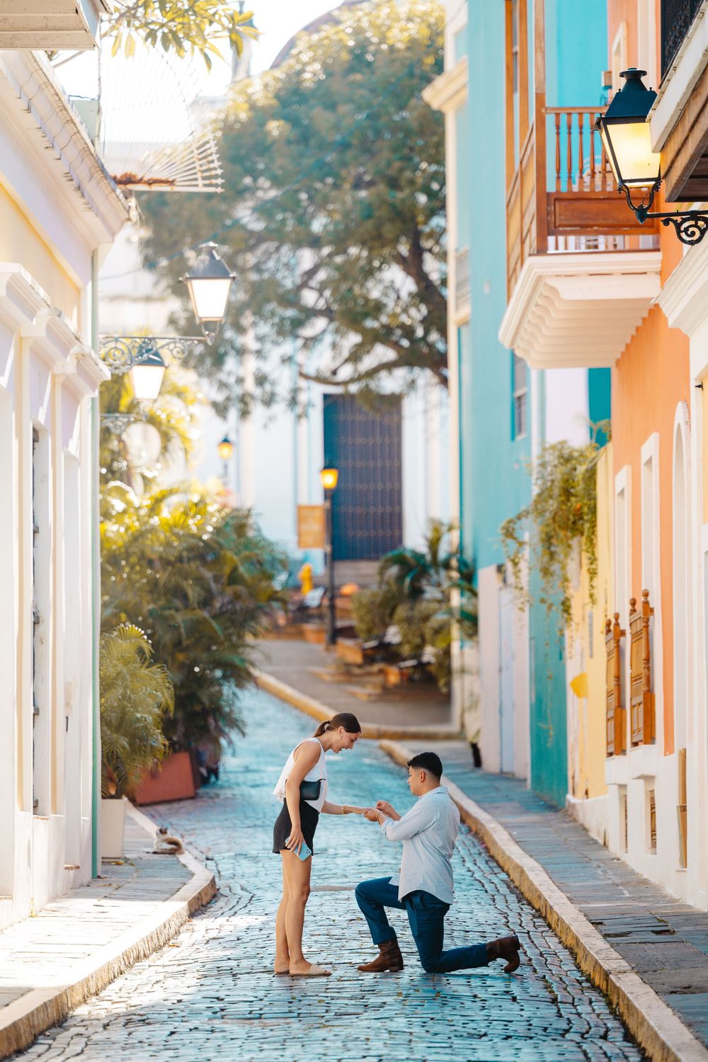 Man proposing on one knee to woman on charming colorful cobblestone street in Old San Juan.