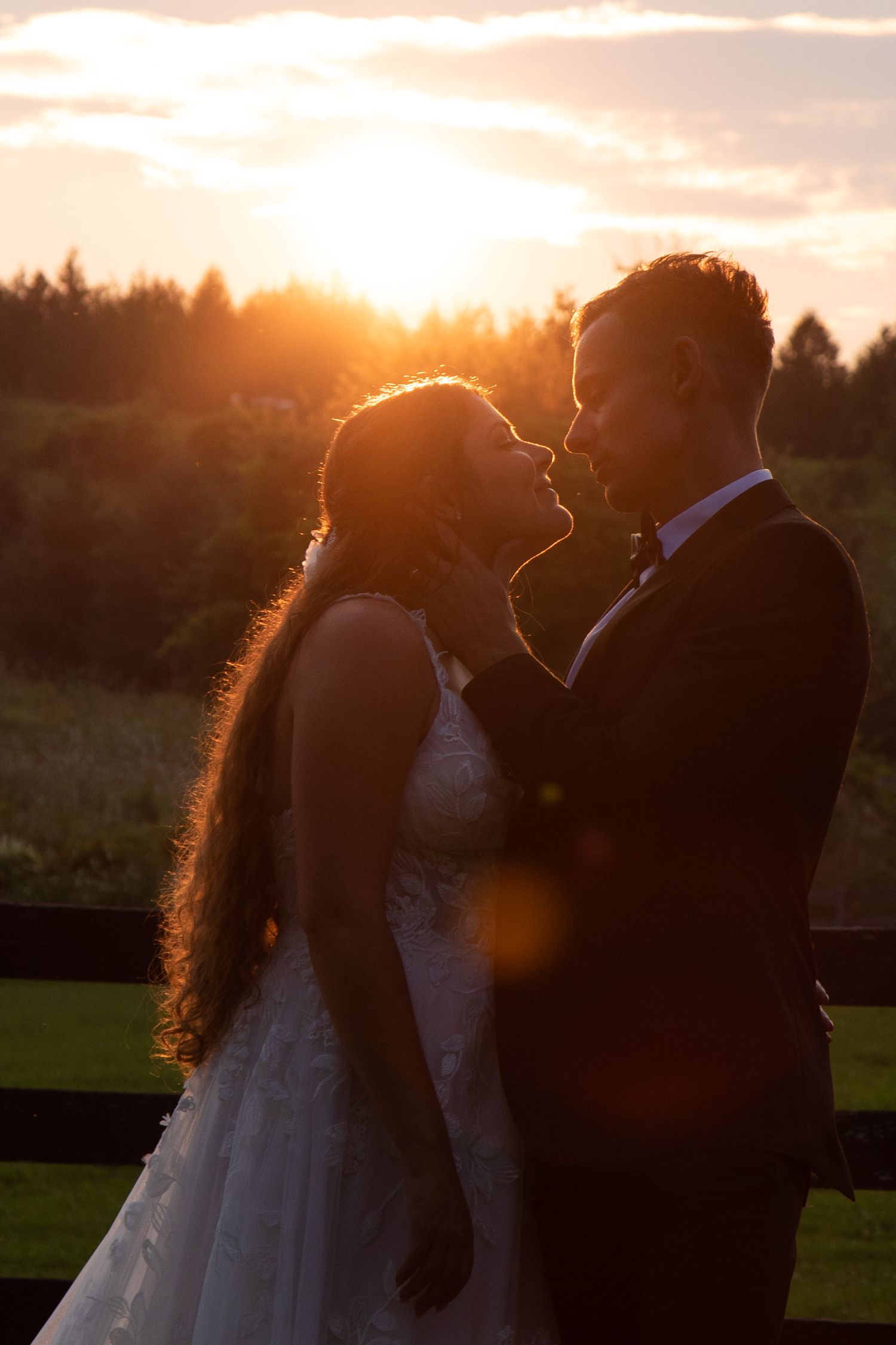 A wedding couple embraces in a golden field during sunset with dramatic clouds overhead.