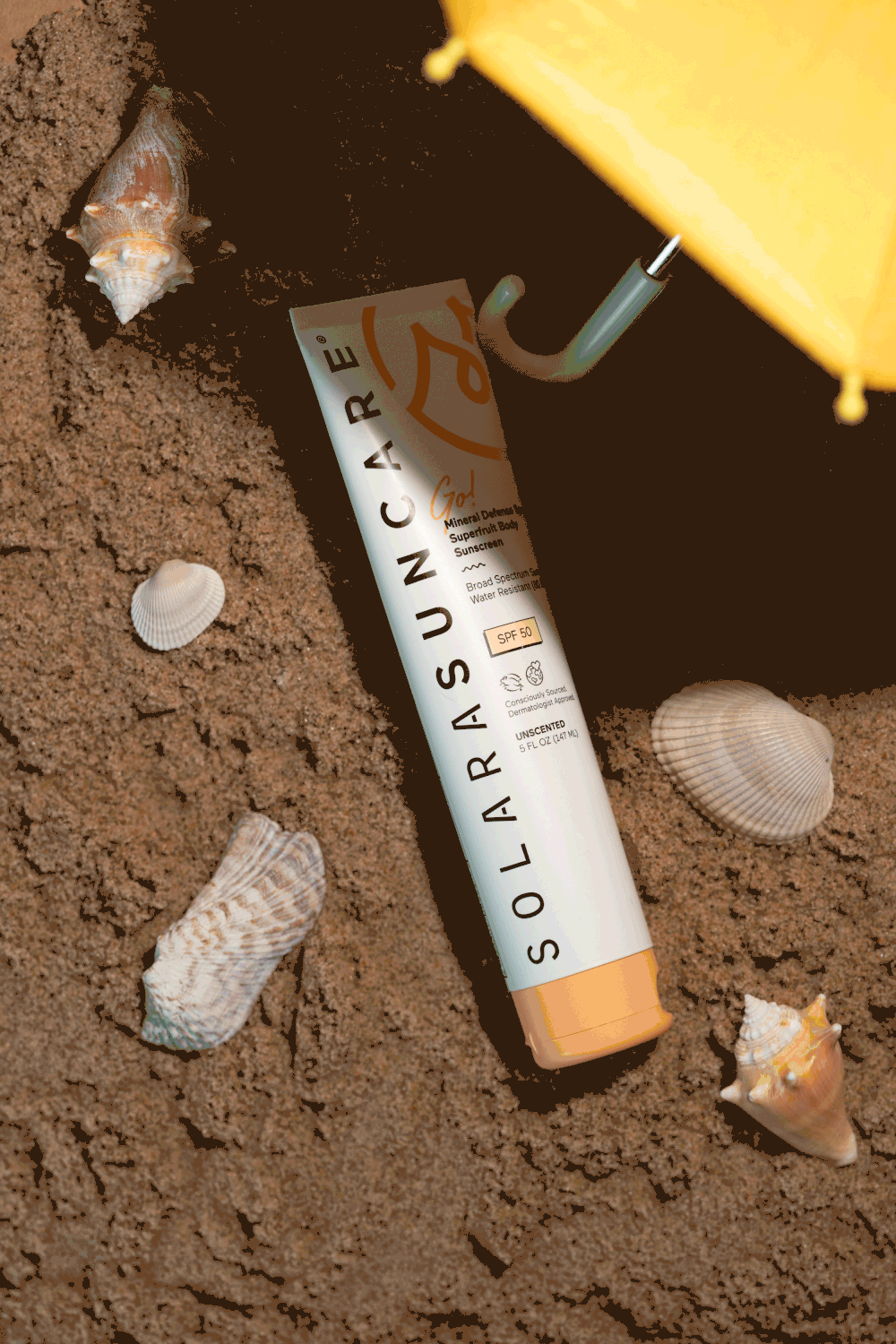 Solara Suncare SPF sunscreen tube lying on sandy beach with seashells and a small yellow umbrella.