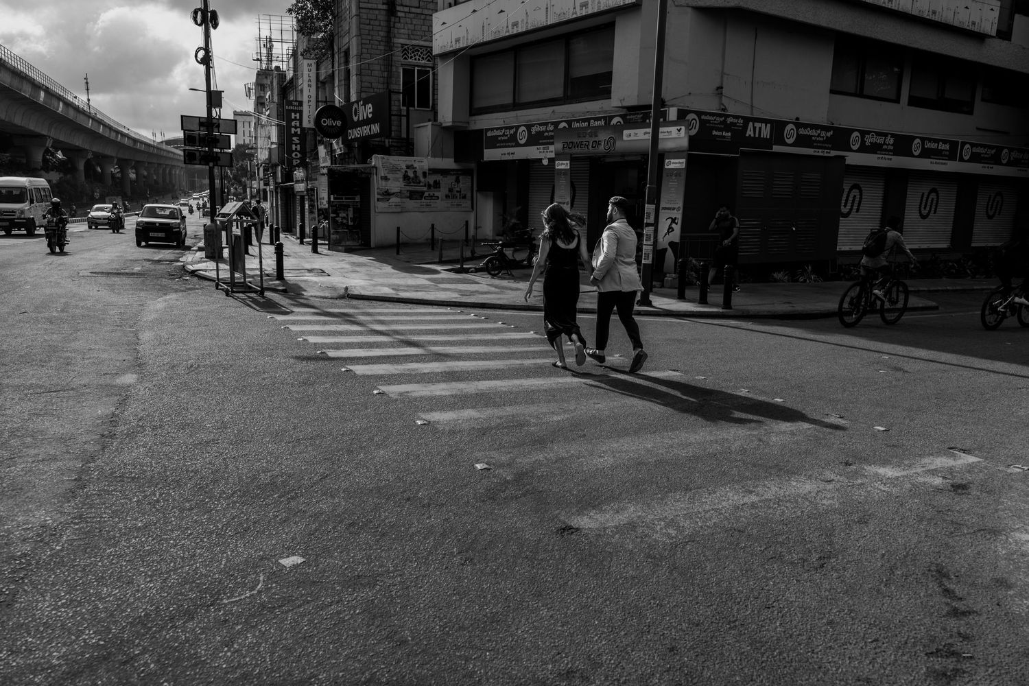 Black and white street scene with pedestrians crossing an urban intersection.