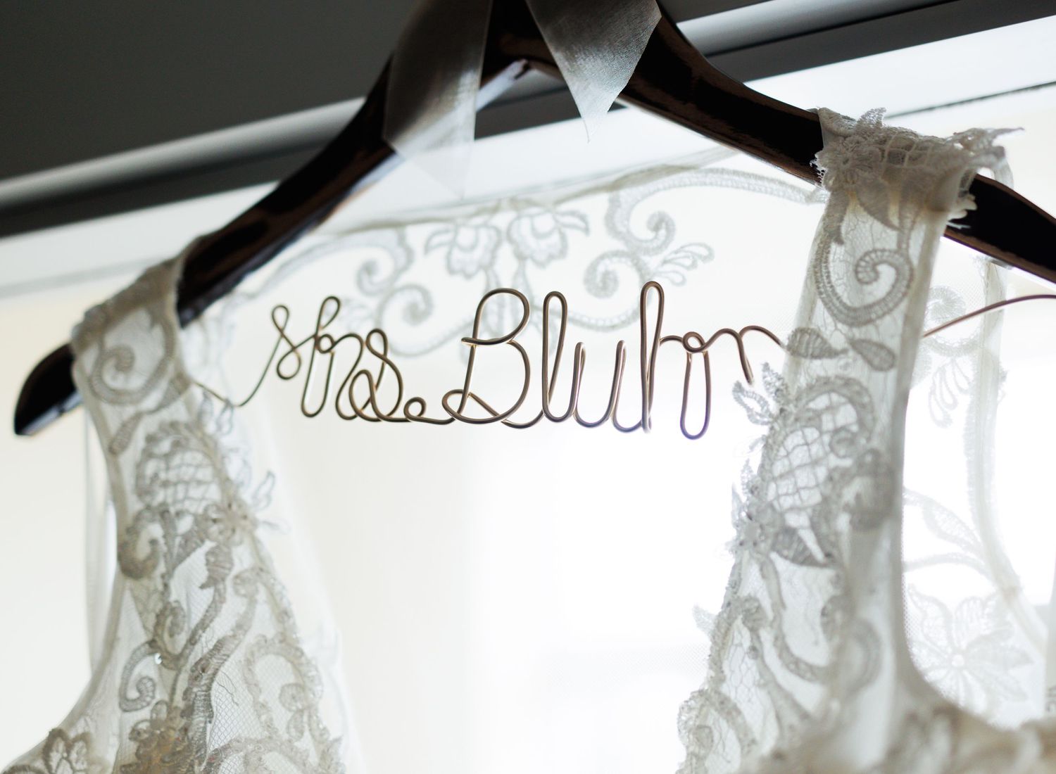Wedding dress hanging on personalized wire hanger with delicate lace details.