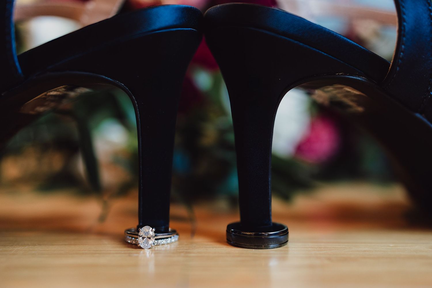 Wedding rings photographed between blue high heels with artistic bokeh background.
