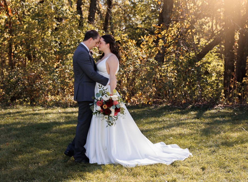 Newlyweds share intimate moment in sunlit forest setting with bride holding red bouquet.