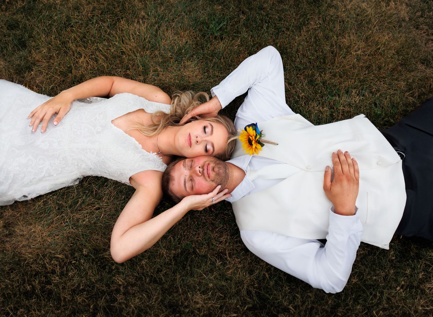 Playful overhead shot of newlyweds lying on grass with yellow flower accents.