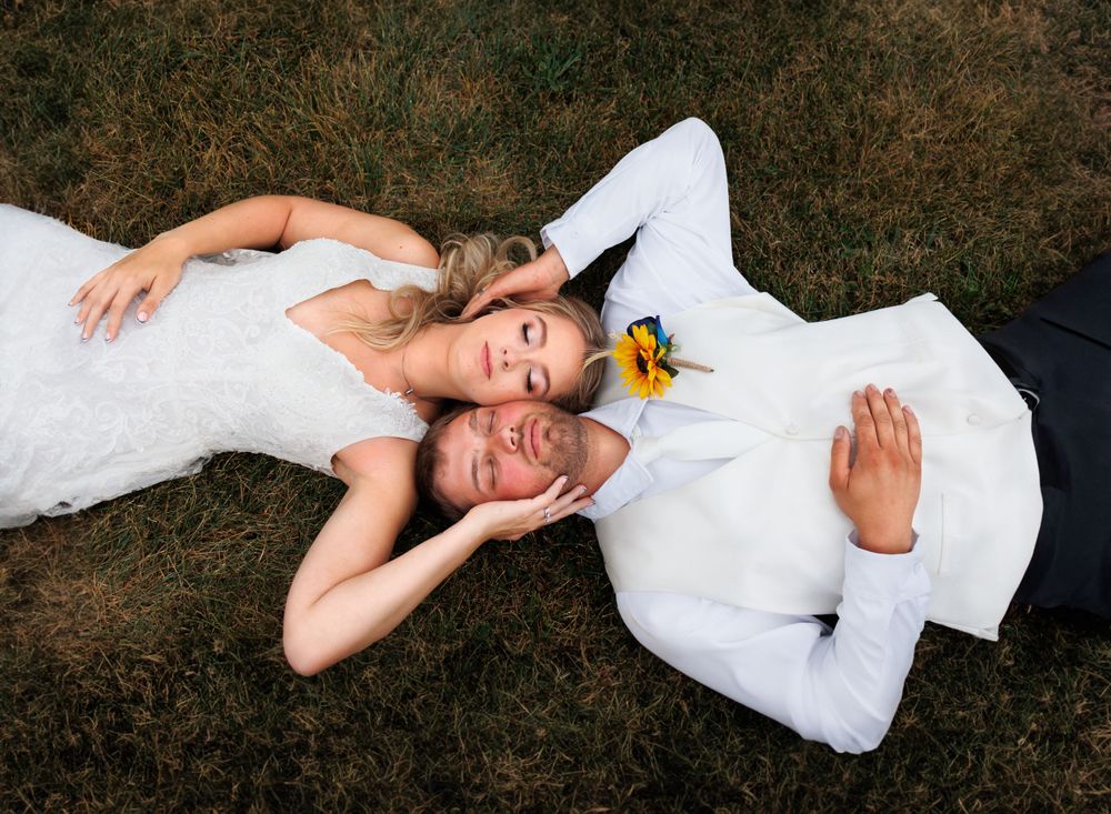 Playful overhead shot of newlyweds lying on grass with yellow flower accents.