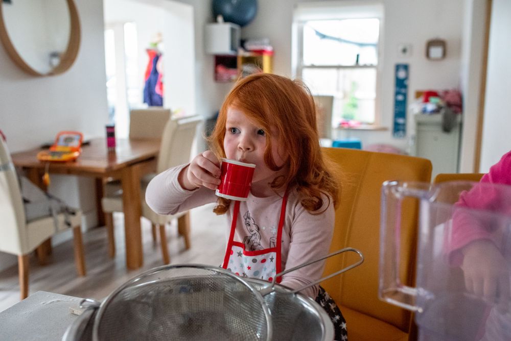 Child in red apron standing at kitchen counter with mixing bowl.