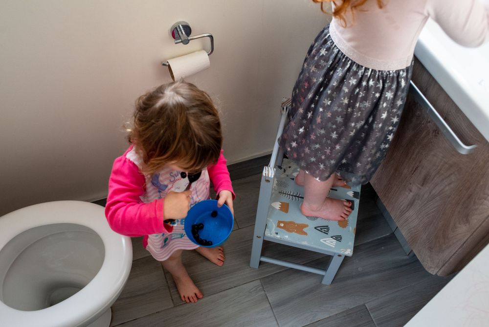Young person using step stool to reach bathroom sink while cleaning.