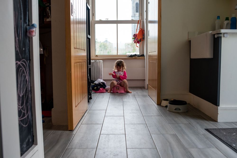 Child sitting alone on tiled floor in hallway near window.