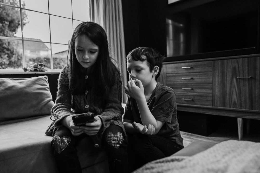 Two people looking at handheld device while sitting by window.