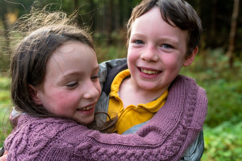 Two children sharing a joyful moment outdoors wearing cozy winter clothing.