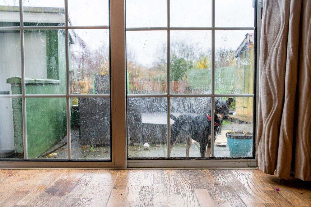 Rainy view through modern window panes with wooden flooring in foreground.