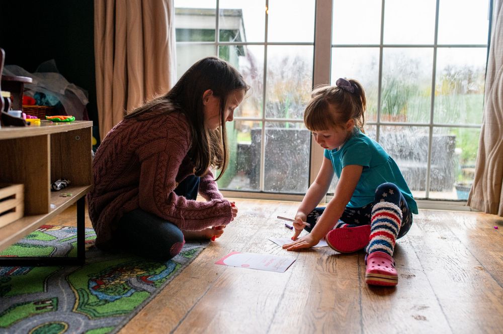 Adult and child sitting on floor playing together near large window.