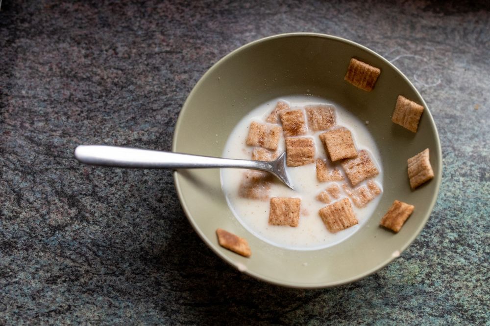 Bowl of cereal with square shaped pieces floating in milk.