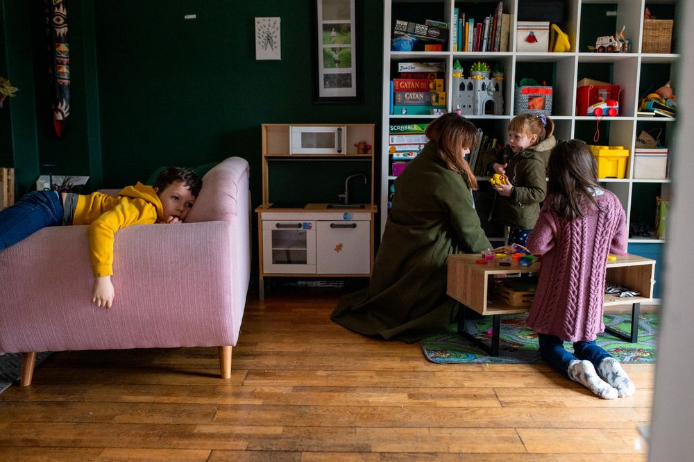 Family gathered in living room with colorful bookshelves and pink couch.