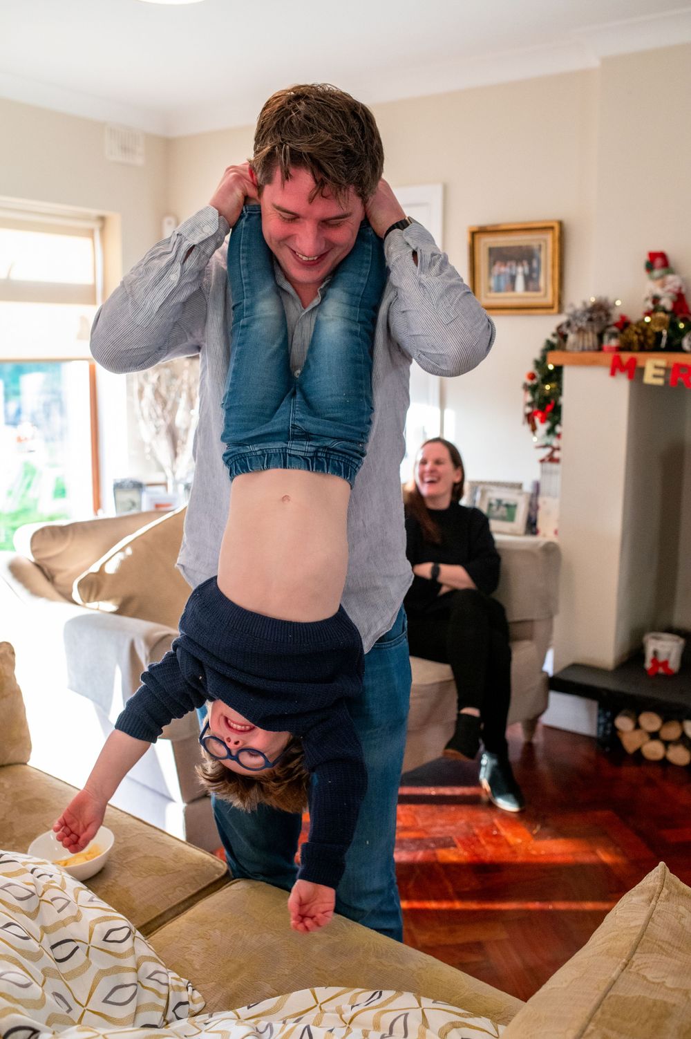 Adult playfully dangling child upside down on couch during family playtime.