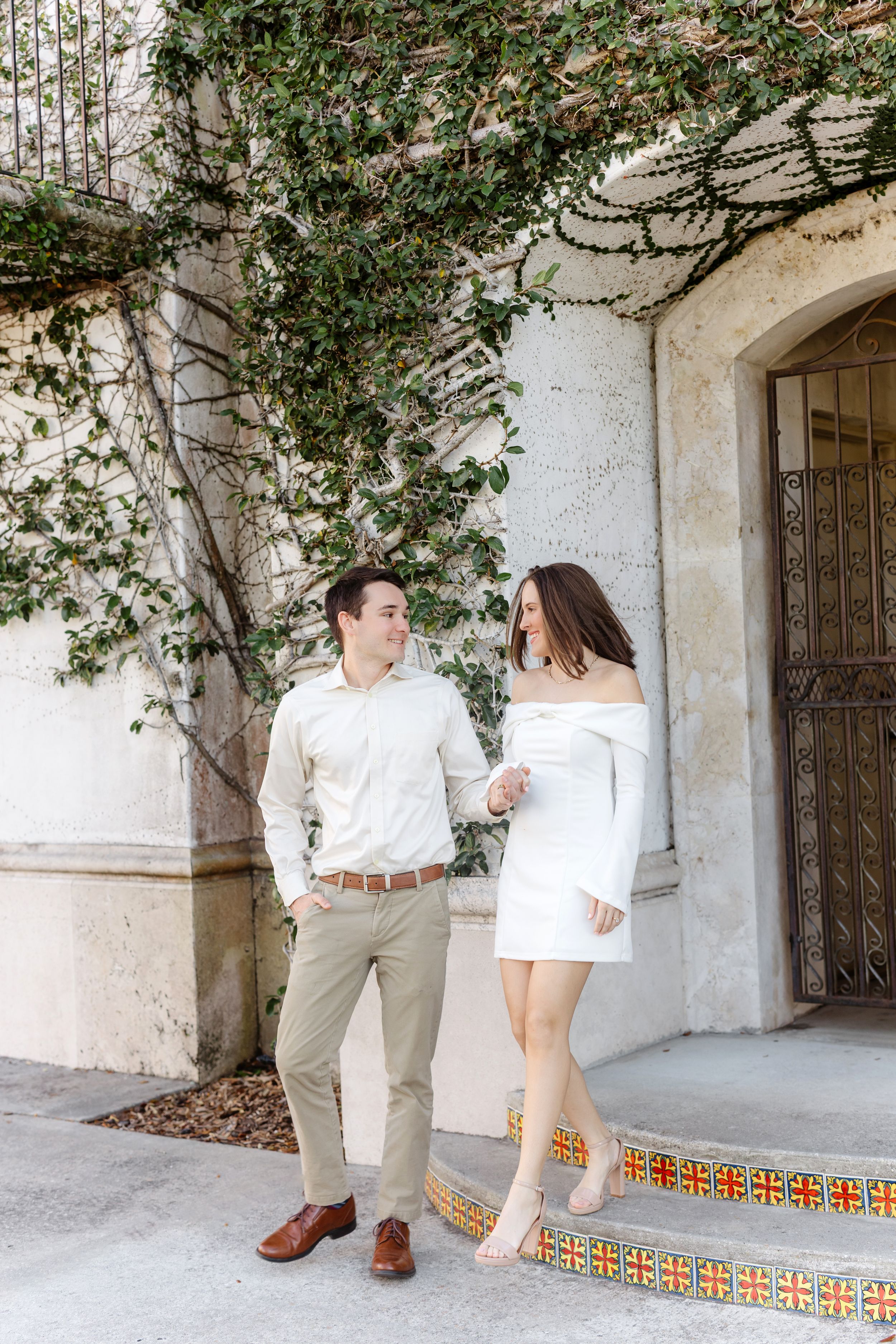 Couple in white and beige outfits share romantic moments along a Spanish-style building with decorative tile steps.