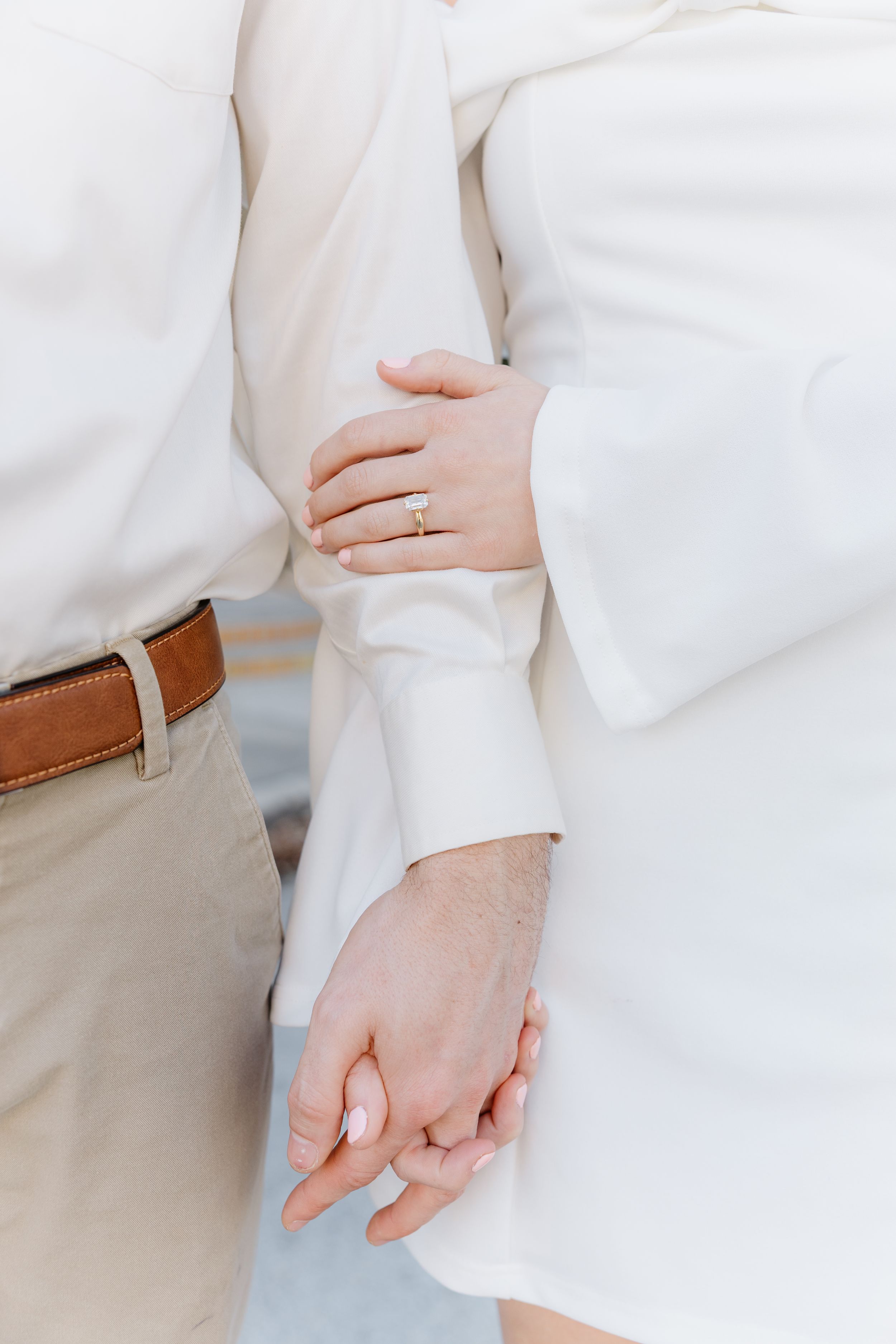 Close-up view of hands wearing a white dress shirt and khaki pants against a light background.