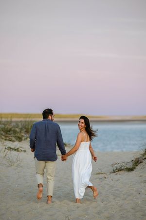 Couple walking barefoot along a beach at sunset holding hands.