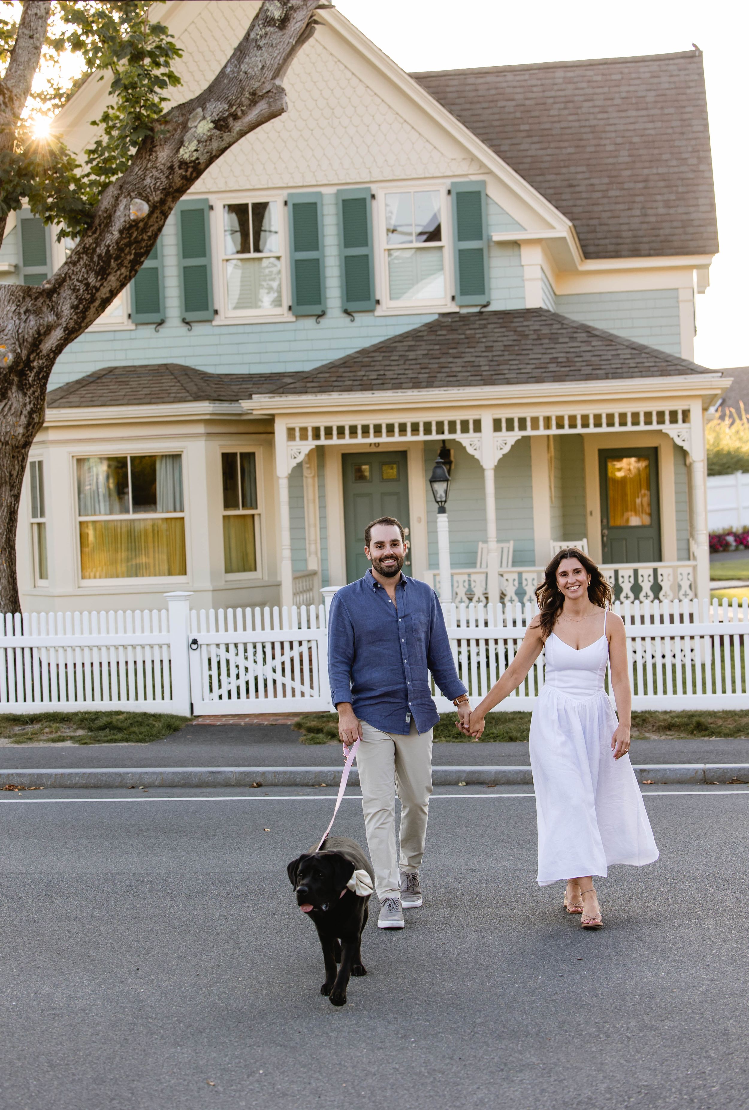 Couple walking along a street in front of a classic white house with a wraparound porch.