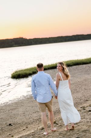 Couple walking along beach shoreline during sunset. New England engagement photos.