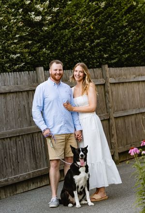 Couple poses with their black and white dog in backyard garden setting. New England engagement photos.