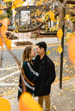 A romantic autumn scene with a couple sharing a tender moment among falling yellow leaves in a park setting. Philadelphia engagement photos.