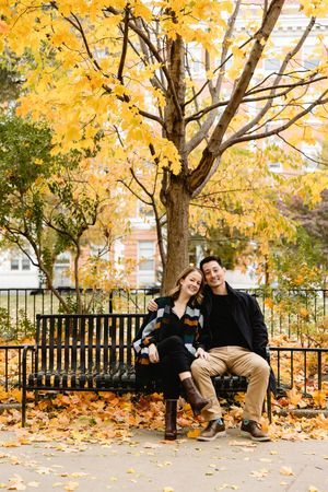 Couple sitting on bench surrounded by vibrant yellow fall foliage. Philadelphia engagement photos.