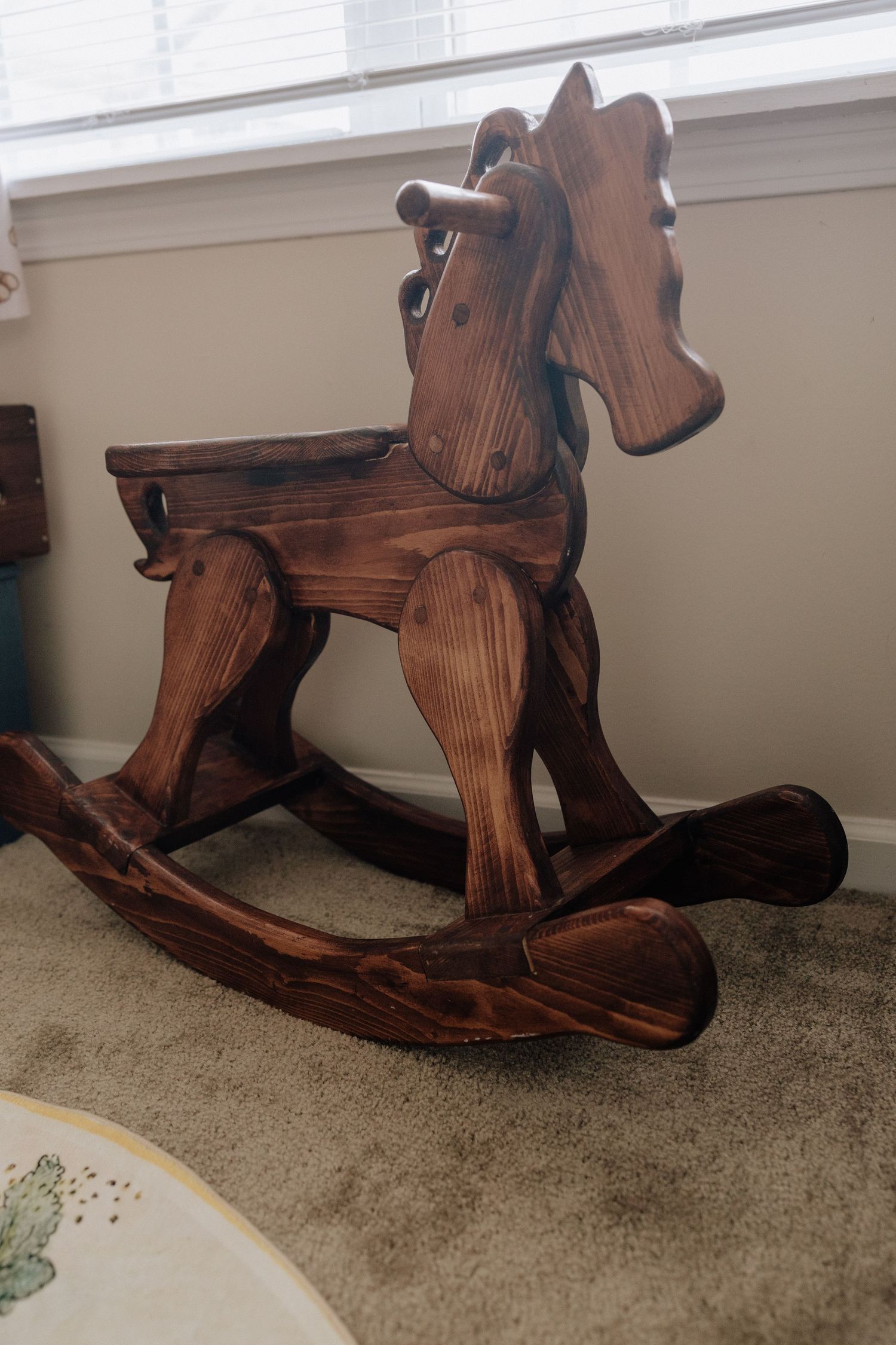 Handcrafted dark wood rocking horse toy on carpet, perfect vintage nursery decor for toddlers.